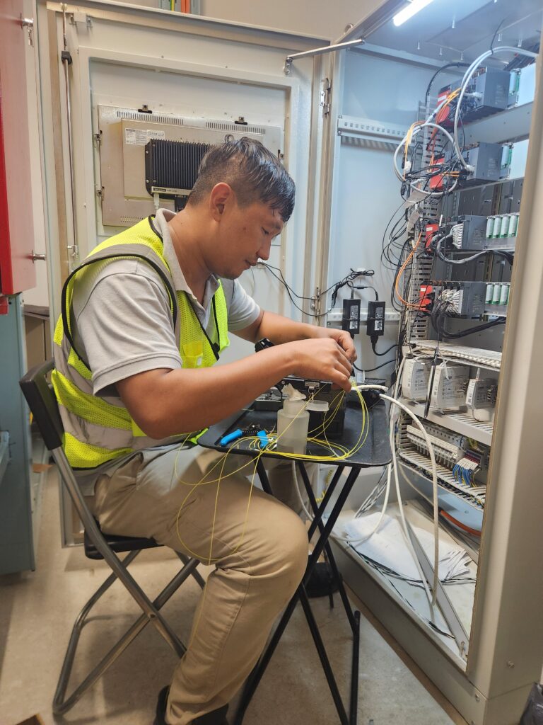 Technician performing fiber optic fusion splicing inside industrial control panel in Singapore